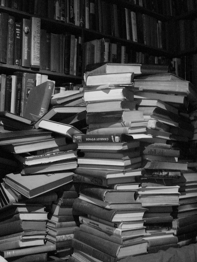 Zwart-witfoto van stapels oude boeken voor een volle boekenkast.